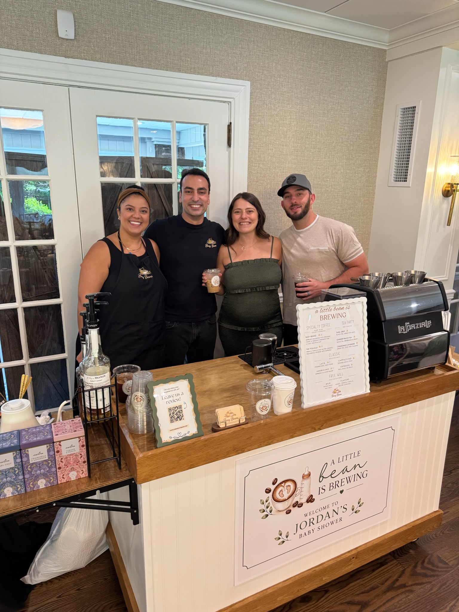 Busy Beans cart with a custom 'A Little Bean Is Brewing' sign at a baby shower, with the hosts and baristas