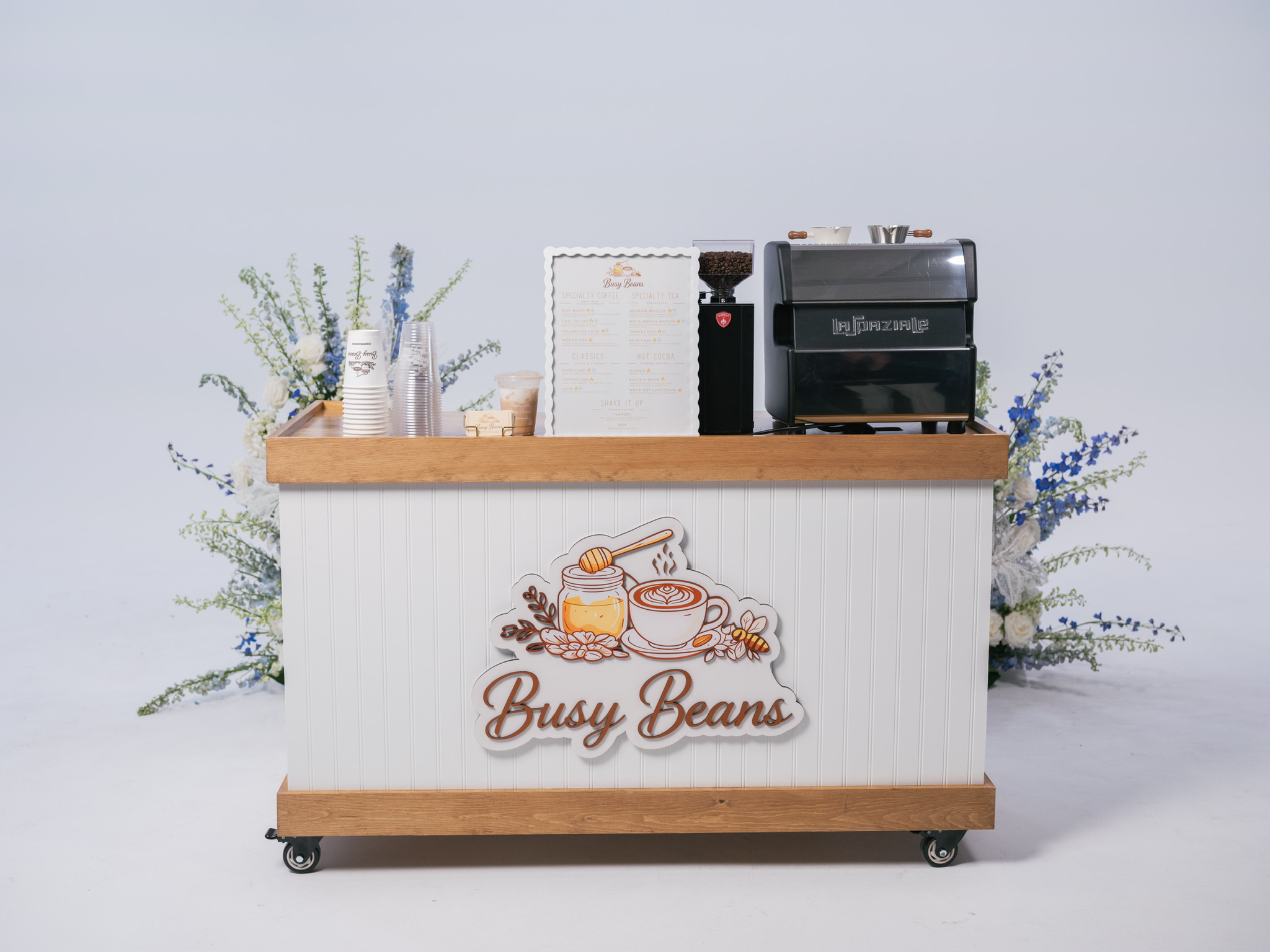 Busy Beans mobile coffee cart with La Spaziale espresso machine, floral arrangements behind it